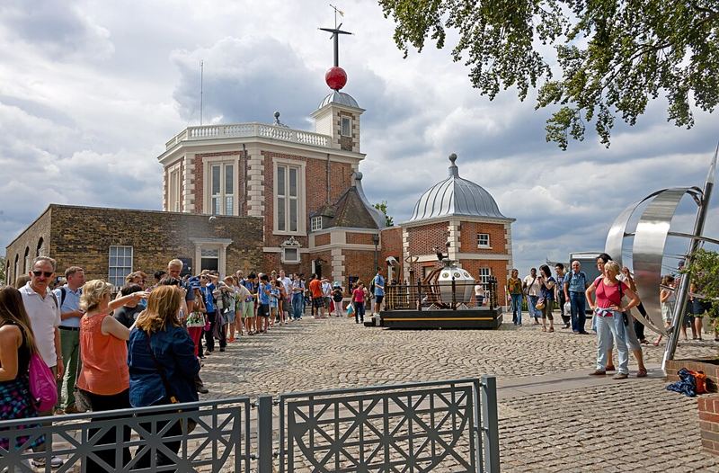 Tourists lining up to take photos on the Prime Meridian line in the courtyard of the Royal Observatory, Greenwich, London