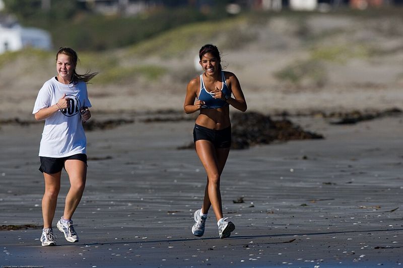 Two women jogging side by side on a beach, smiling