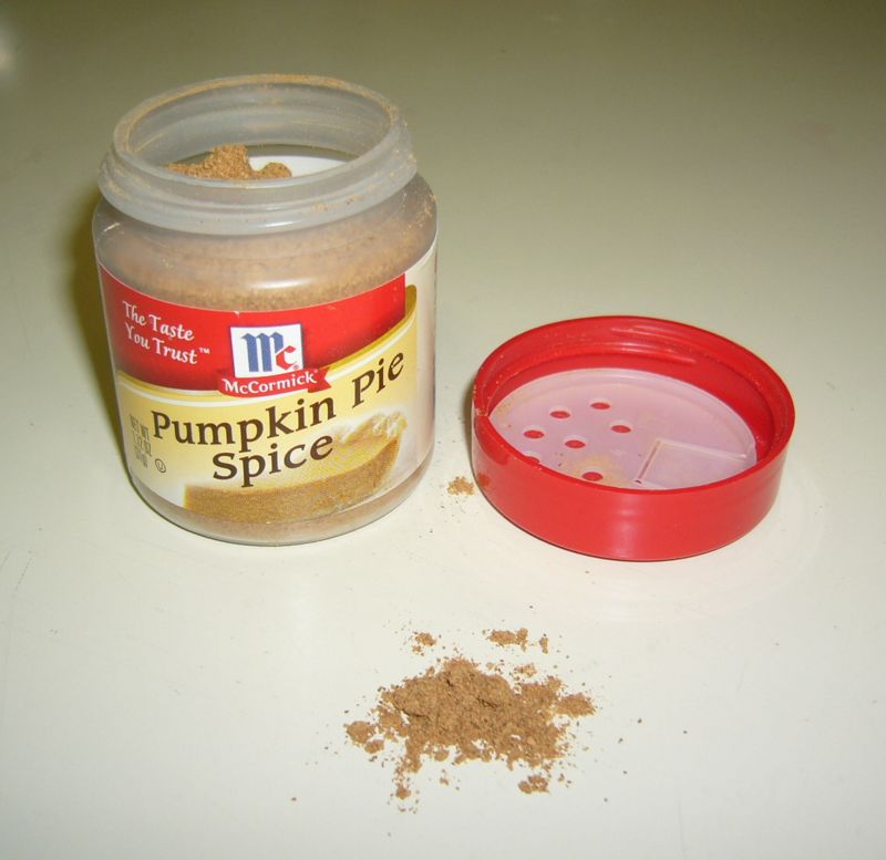 An open jar of McCormick Pumpkin Pie Spice with its red lid and a small pile of the ground spice blend