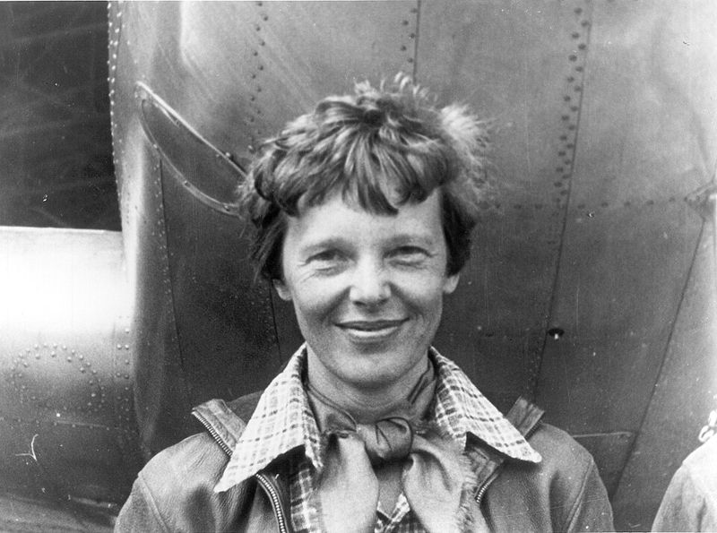 Amelia Earhart standing under the nose of her Lockheed Electra airplane, 1937 (public domain photo)