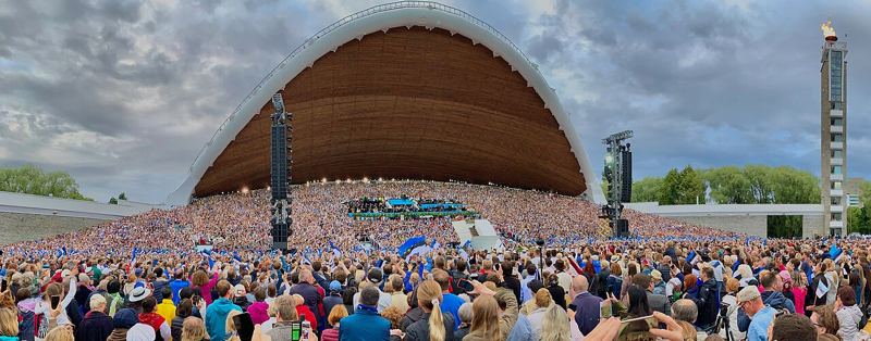 Large crowd waving Estonian flags in front of the arched song stage at the 2019 Estonian Song Festival in Tallinn