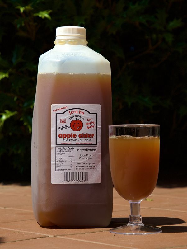 A half-gallon jug of pasteurized Jericho Cider Mill apple cider labeled keep refrigerated, next to a glass of cider