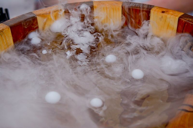 White fog billowing from dry ice pellets in a wooden bowl of cold water