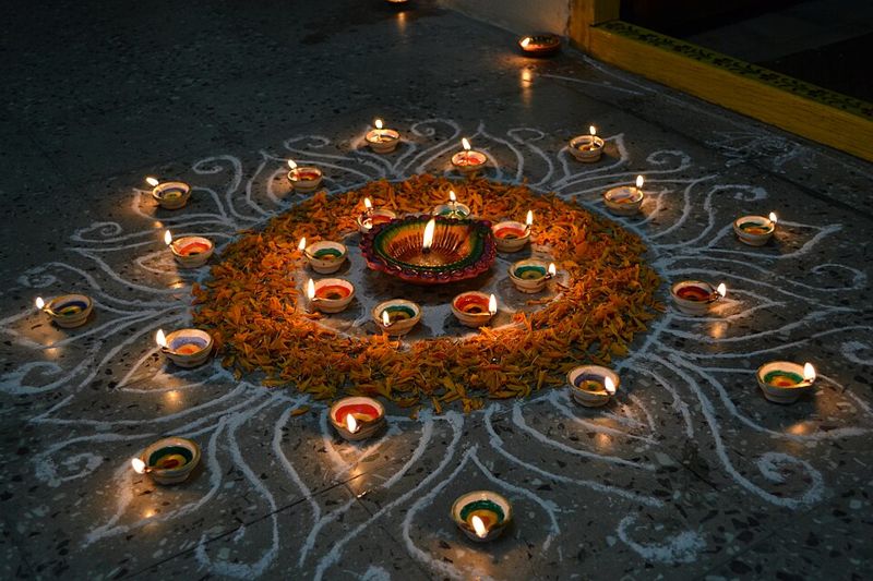 Lit clay diya oil lamps arranged in a circle around a marigold-petal rangoli on a floor at night