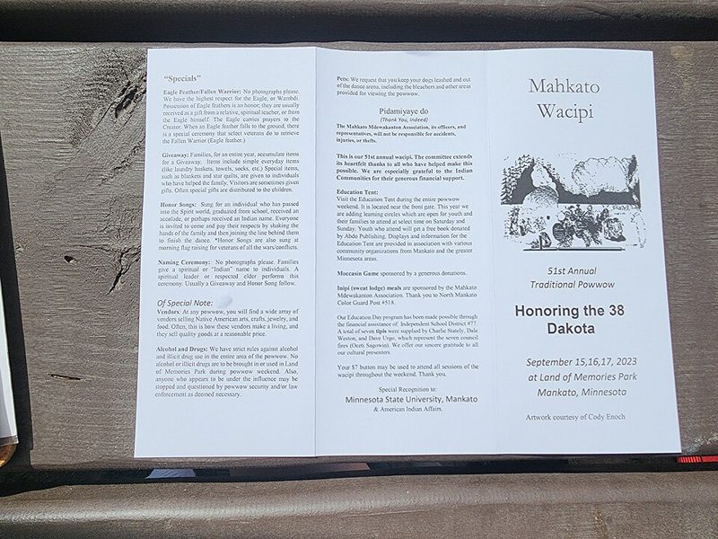 A printed trifold event program brochure laid open on a wooden bench